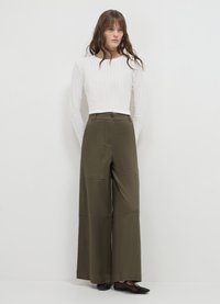 Maglietta bianca a maniche lunghe a coste abbinata a pantaloni olivo a vita alta e gamba larga, con tasche frontali e chiusura con bottone. Scarpe nere.