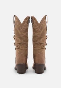 Botas de vaquero de ante marrón con un diseño arrugado, puntas afiladas, cremalleras laterales y tacones apilados. Detalles de costura sutil en los laterales.