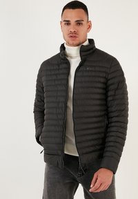 Piumino nero con motivo a righe orizzontali, colletto alto, zip completa e tasche laterali. Indossato sopra un leggero dolcevita.