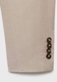 Beige tailored trouser cuff with a diagonal weave texture, featuring four dark buttons with a glossy finish and contrasting thread.