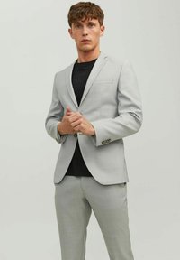 Light gray suit made of textured fabric, featuring a single-button jacket with a pocket and matching tailored trousers over a black shirt.