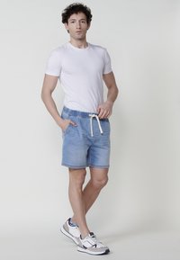 Jeansshorts i ljusblått med elastisk midja och dragsko, ihop med en tajt vit t-shirt och vita sneakers.