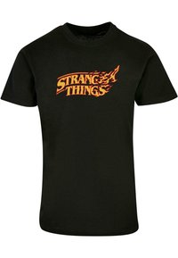Juoda medvilninė marškinėlių su trumpomis rankovėmis, turinti ugnies stiliaus "STRANGER THINGS" logotipą oranžinės ir geltonos spalvų, apvaliu kaklu.