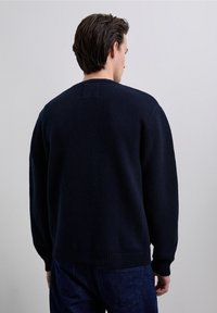 Navy sweater with a round neckline, ribbed cuffs, and hem. The fabric appears knitted, and the back features a smooth finish without patterns.