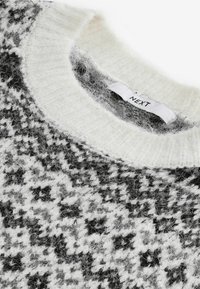 Pull tricoté noir et blanc avec une texture duveteuse, un col rond et une étiquette indiquant "NEXT". Motif pied-de-poule distinctif visible.