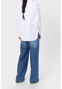 Valkoinen pellavapaita, jossa on hieman kaareva helma, yhdistettynä avarahelmaisiin sinisiin denim-farkkuihin, joissa on haalistunut pesu ja minimaalinen ompelu.