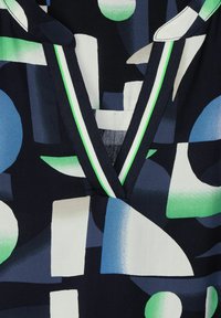 Tessuto astratto colorato con un fondo navy e forme geometriche blu, verdi e bianche. Design a V con accenti verdi.