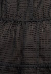 Μαύρο διαφανές ύφασμα με οριζόντια και κατακόρυφη υφή πλέγματος, μαζεμένο στις ραφές δημιουργώντας ελαφριές πτυχώσεις και όγκο.