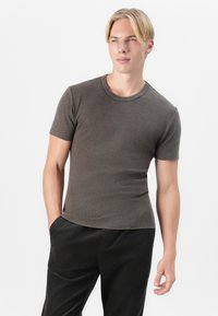 Short-sleeved, fitted dark brown ribbed t-shirt with a round neckline, paired with black corduroy pants, hands in pockets.