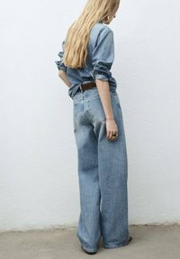 Jean en denim bleu clair avec une taille haute et des jambes larges, associés à une chemise en denim bleue avec des manches retroussées.