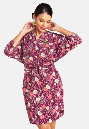 Lila Kleid mit floralen Mustern in Rot und Grün, mit Taillenschleife, lockeren Ärmeln und einem kragenlosen Ausschnitt.