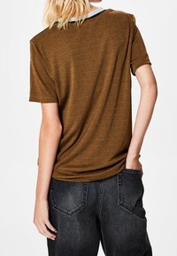 Brun kortærmet t-shirt lavet af blødt stof med rund halsudskæring og sorte detaljer. Bæret med mørke grå højtaljede jeans.