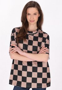 Camiseta de manga corta con un gran patrón a cuadros en negro y beige. Tejido suave y liso con cuello redondo y corte relajado.