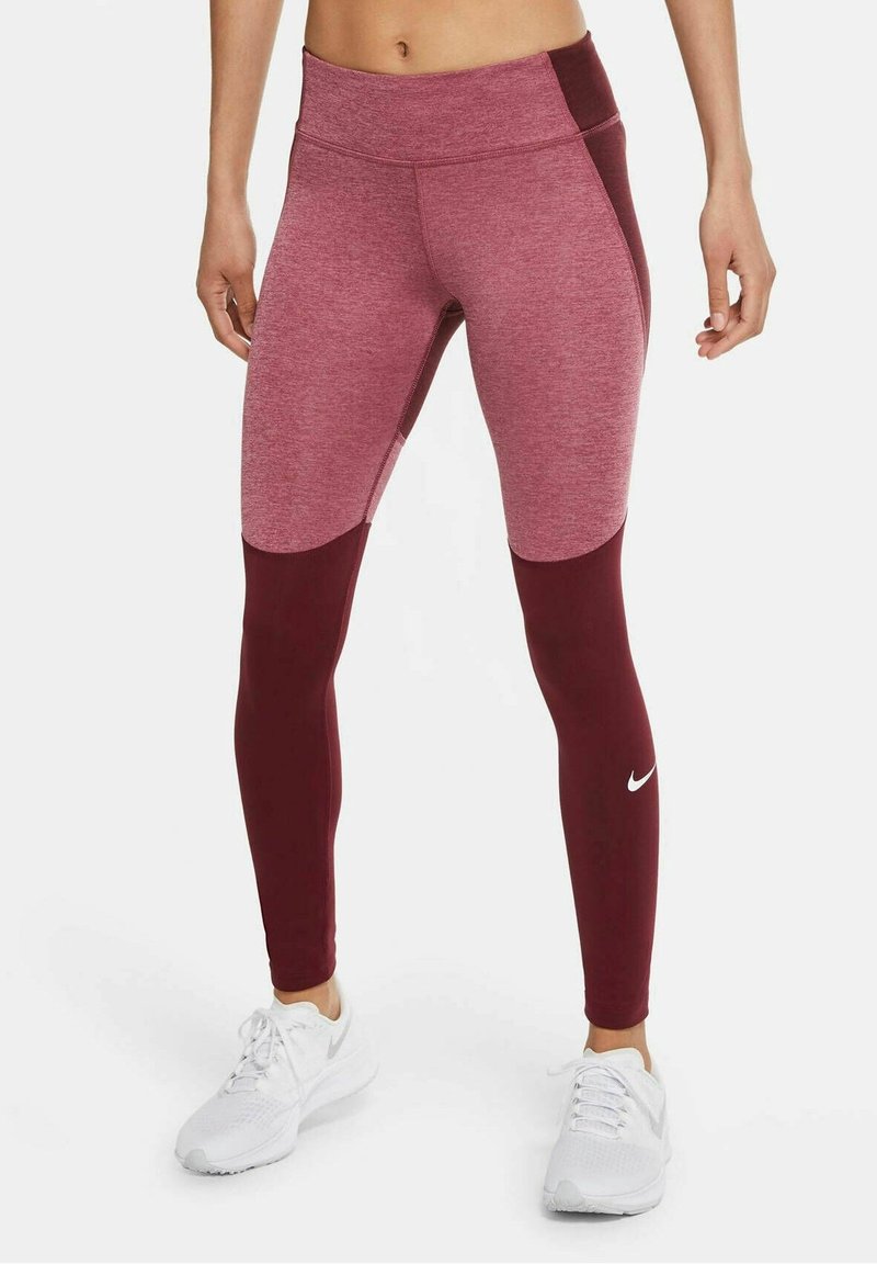 Tights tillverkade av en texturerad blandning i burgundnyanser, med hög midja och en accentpanel, kombinerat med vita träningsskor.