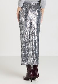 Gonna midi in paillettes argento con righe verticali di paillettes lucide, caratterizzata da una silhouette dritta. Abbinata a stivali alti fino al ginocchio di colore bordeaux.