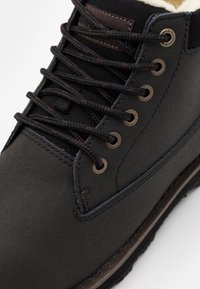 Bota de cuero negro con ojales plateados, cordones gruesos y un upper texturizado. Cuenta con un forro interior suave y una suela duradera.
