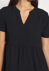 Black dress featuring a V-neckline, short sleeves, and a gathered waist for a flared silhouette. Fabric appears soft and textured.