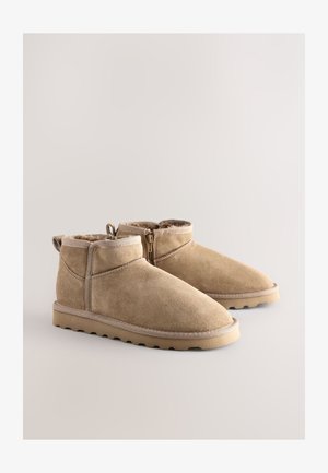 Bézs színű velúr bokacsizma cipzárral, puha belső béléssel és mintás gumitalppal a jobb tapadásért. Minimális varrási részletekkel.