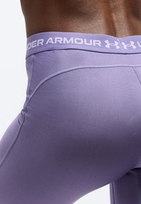 Κοντινό πλάνο ενός ατόμου που φορά στενά βιολετί κολάν Under Armour, με το λογότυπο της μάρκας να εμφανίζεται στη μέση.