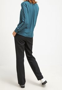 Tyrkis blus med långa ärmar och bakfåll, i kombination med svarta byxor och kraftiga skor med vit sula. Enkelt mönster med rena linjer.