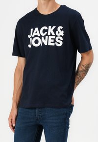 Granatowa bawełniana koszulka z krótkim rękawem, z wyrazistym białym napisem "JACK & JONES" na piersi oraz okrągłym dekoltem.
