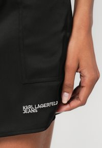Črne kratke hlače iz gladkega blaga z bočnim žepom in belo vezenino "KARL LAGERFELD JEANS" na robu.