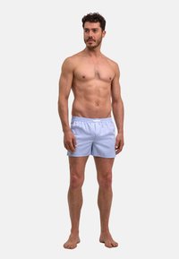 Blauw gestreepte korte broek gemaakt van lichtgewicht stof, met een elastische tailleband en een losse pasvorm, gecombineerd met blote voeten en zonder shirt.