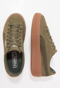 Zelené semišové tenisky s texturovanou hnědou gumovou podrážkou, s polstrovaným límcem, šněrováním a postranními akcenty značky.