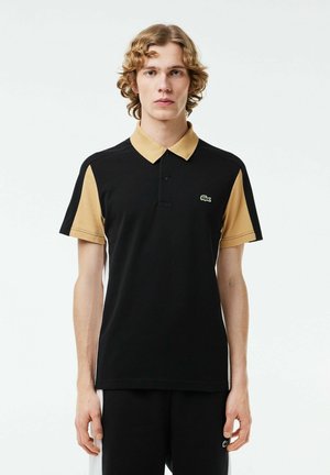Polo negro de manga corta, con acentos en beige y un logotipo de cocodrilo verde en el pecho. Fabricado en material de algodón ligero.