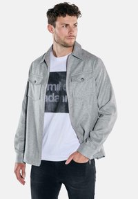 Gray textured jacket with a collared design, featuring two chest pockets and a front zipper. Worn over a white graphic t-shirt.