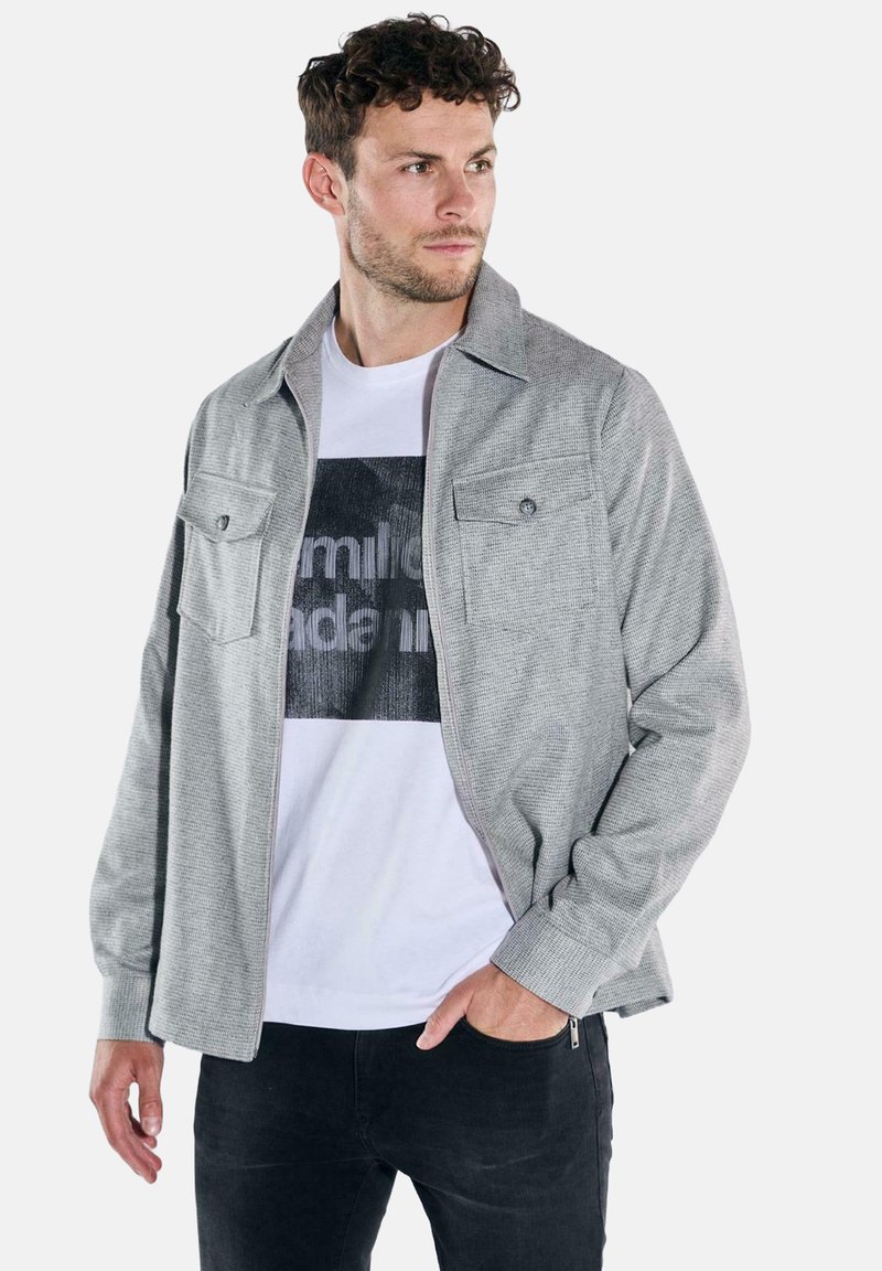 Gray textured jacket with a collared design, featuring two chest pockets and a front zipper. Worn over a white graphic t-shirt.