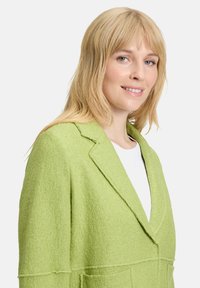 Zielona marynarka z mieszanki wełny o strukturalnym wykończeniu, z klapami w kształcie notched i dwiema przednimi kieszeniami, charakteryzująca się dopasowanym krojem.
