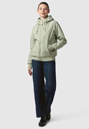 Veste zippée vert menthe avec capuche, poches latérales et poignets élastiques, portée avec un jean large bleu foncé et des bottes noires à lacets.