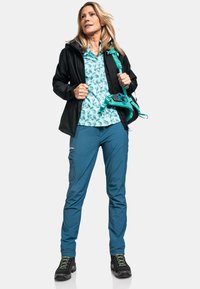 Outdoor-Bekleidung mit einem blauen Blumenhemd, einer schwarzen wasserdichten Jacke und blauen Hosen. Zubehör umfasst eine türkisfarbene Hüfttasche. Schwarze Wanderschuhe.