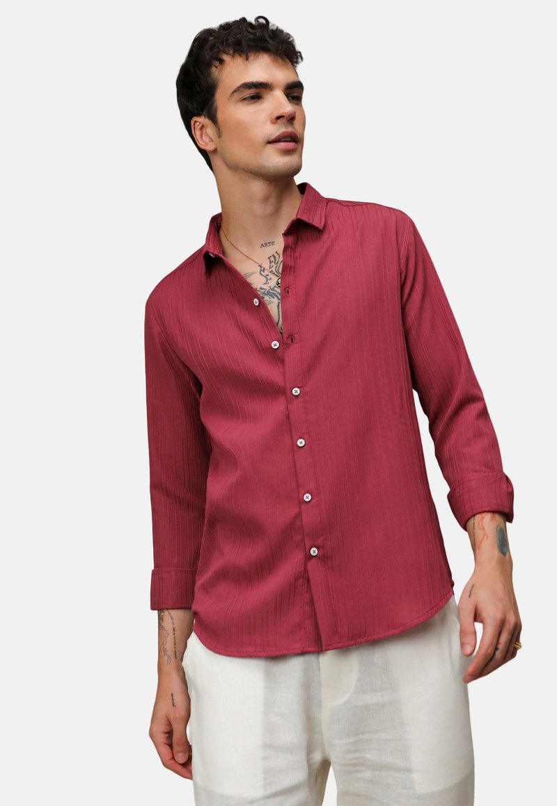 Camicia a maniche lunghe a righe rosse, con una vestibilità comoda e un orlo leggermente curvo. Indossata con pantaloni di colore chiaro.