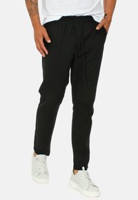Pantaloni jogger neri con vita elastica e lacci, caratterizzati da una vestibilità slim e caviglie cimose, abbinati a sneakers bianche.