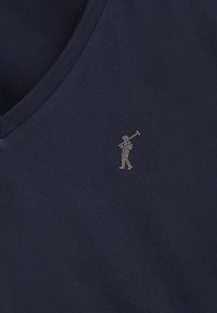 Marinblå bomull t-shirt med V-ringning som har en liten metallisk strassgolfergrafik på vänster bröst. Mjuk textur, avslappnad design.