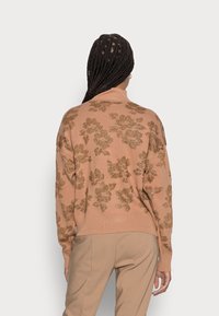 Pull pêche tricoté avec un col haut, orné de motifs floraux dorés scintillants. Poignets et ourlet côtelés, coupe décontractée.