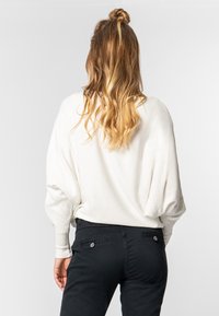 Witte trui met losse, ballonmouwen, gecombineerd met zwarte broek met twee achterzakken en knoopaccenten. Zachte textuur, casual pasvorm.