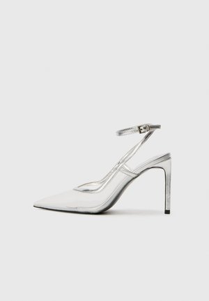 Klare stiletthæl sko med spids tå, gennemsigtigt materiale, metallisk sølvdetaljer og justerbar ankelrem.