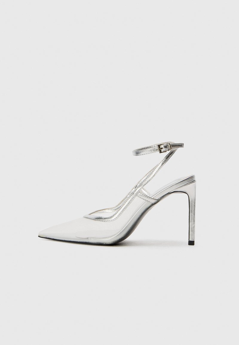 Klare stiletthæl sko med spids tå, gennemsigtigt materiale, metallisk sølvdetaljer og justerbar ankelrem.