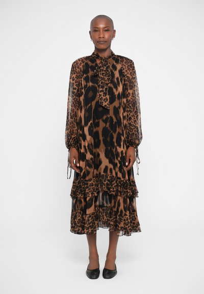 Kleid mit braunem Leopardenmuster, langen Ärmeln, Rüschen am Saum und einem Nackenband. Der Stoff sieht leicht und durchscheinend aus und wird mit schwarzen Ballerinas getragen.