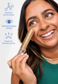 Lächelnde Frau hält ein Essential Lash Serum in der Hand, mit Symbolen, die Biotin, Aminosäuren, augenärztlich getestet und natürliche Wimpernunterstützung hervorheben.