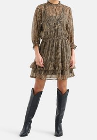 Braun und schwarz gestreiftes Kleid mit Rüschensaum, langen Puffärmeln und hohem Hals, kombiniert mit schwarzen knielangen Stiefeln.