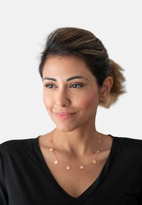 Rosaguld halskæde med runde vedhæng på en delikat kæde, båret med en sort V-hals top, med et detaljeret nærbillede af designet.