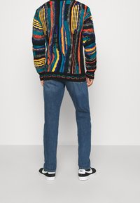 Mustat neuleet, joissa on monivärisiä pystyraitoja, yhdistetty sinisiin farkkuihin ja mustiin tennareihin, joissa on valkoisia yksityiskohtia.