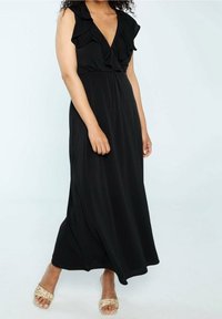 Robe longue noire avec des accents de manches à volants et un décolleté en V plongeant. Tissu doux et fluide, avec une coupe décontractée et des fentes sur les côtés. Portée avec des sandales neutres.