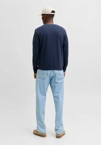 Marineblå sweatshirt med rund hals, kombineret med lyseblå denimjeans. Outfittet har en afslappet pasform og beige slip-on sko.