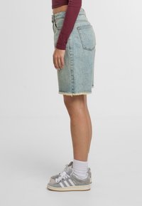 Falda midi de denim en lavado claro con dobladillo deshilachado, combinada con zapatillas grises. El conjunto incluye un top corto de manga larga en color burdeos.