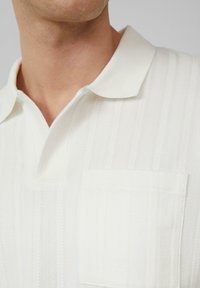 Witte polo t-shirt met een gemarmerd herringbone patroon, korte kraag en een borstzak. Gladde stof met verticale strepen.